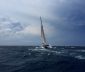 White sail boat, tacking into the headwind, on a body of water.